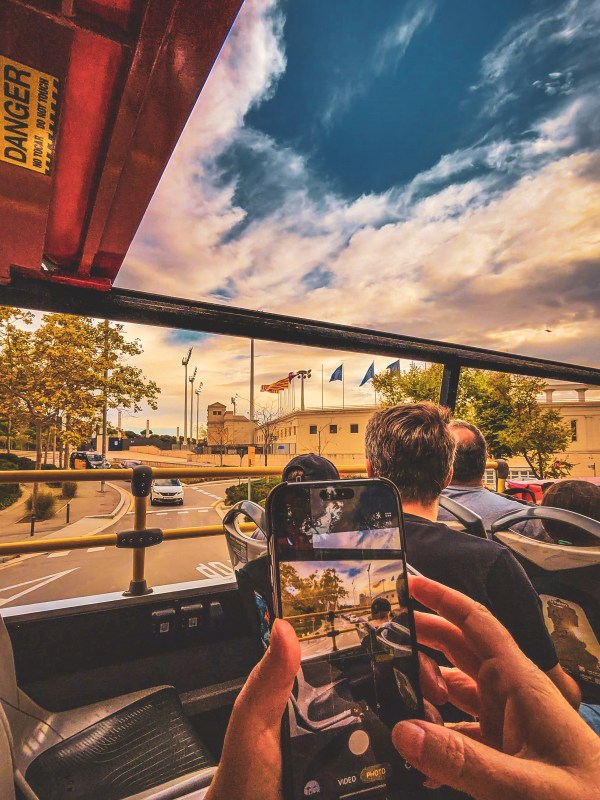 Hands holding smartphones on an open-top sightseeing bus in Barcelona.