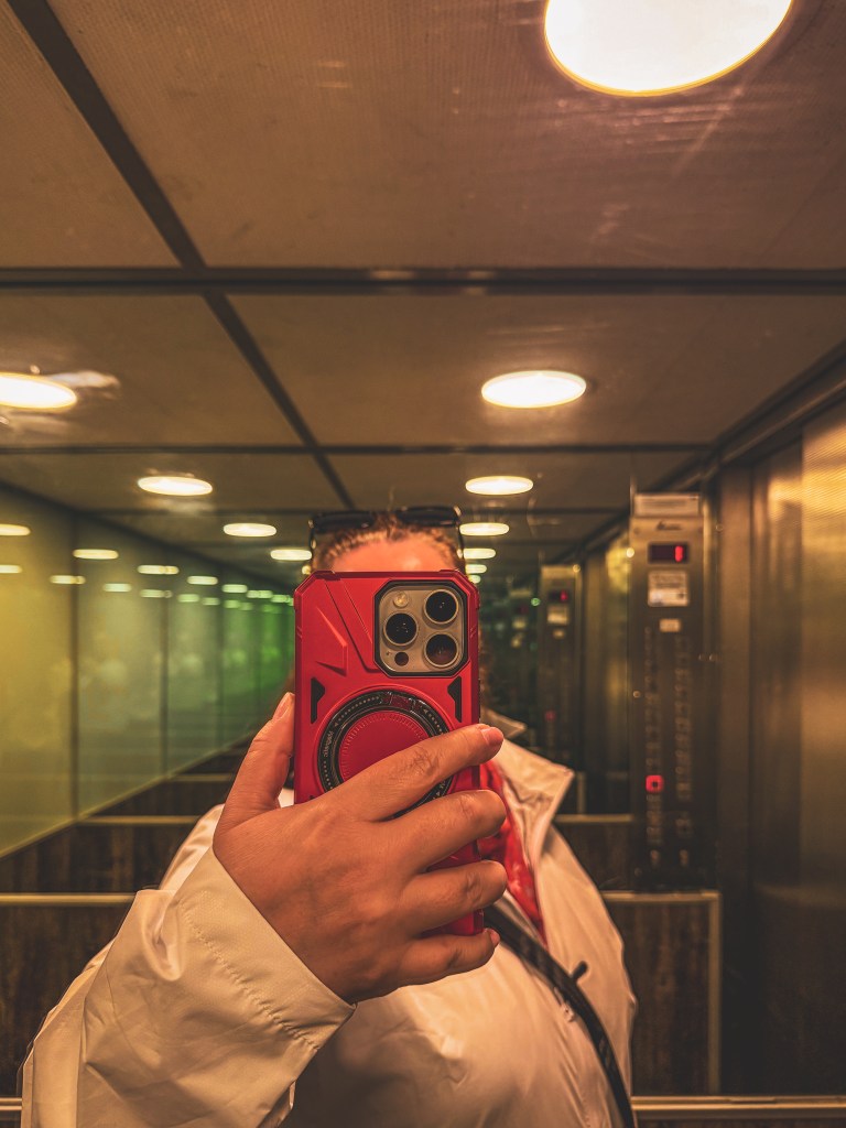 Charlotte photographing her reflection with a smartphone while travelling.