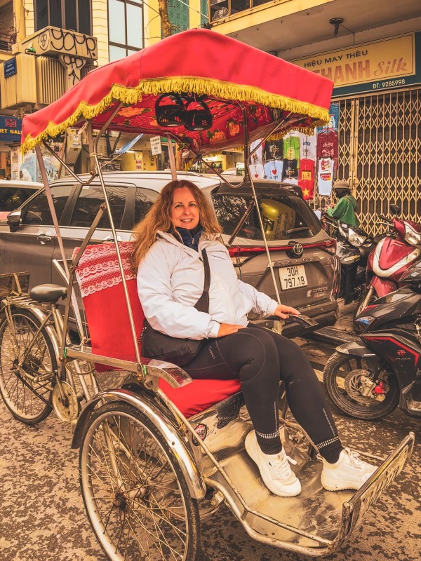 Charlotte seated in a red cycle rickshaw in Hanoi.