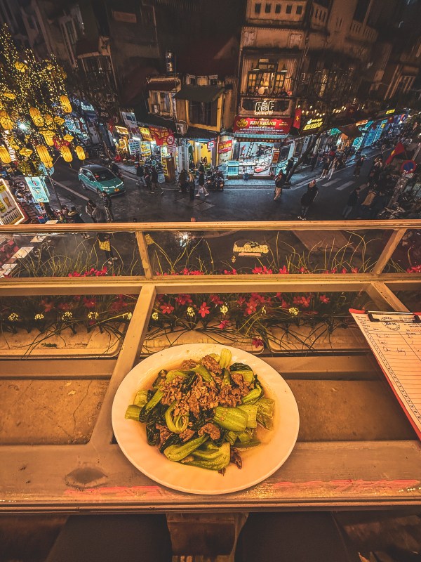 A plated meal on a balcony table overlooking Hanoi at night.