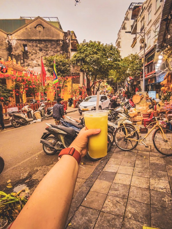 A hand holding a drink above a busy Hanoi street.
