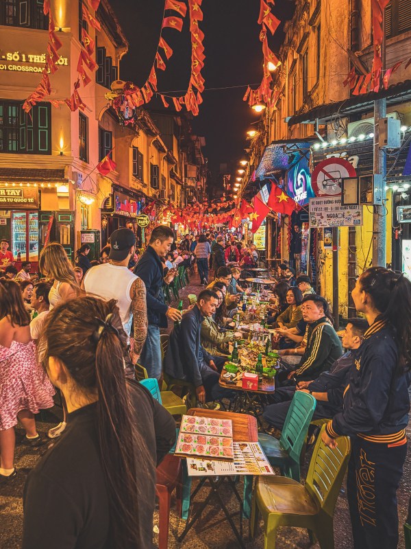 Crowded Hanoi night street beneath hanging flags.