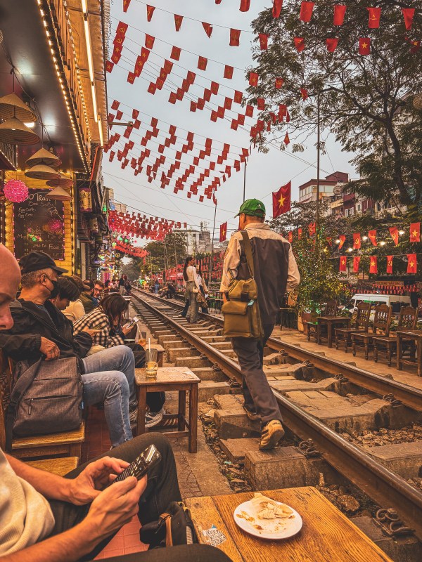People beside railway tracks under flags in Hanoi.