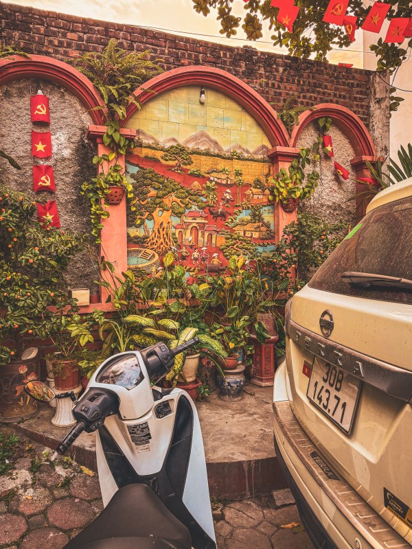 A scooter and car beside an arched wall with foliage in Hanoi.