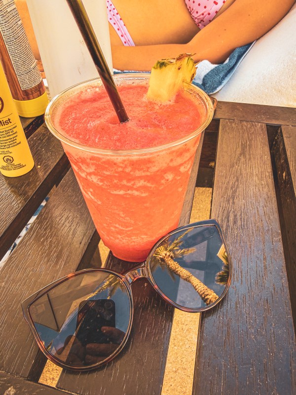 Red cocktail beside sunglasses on an outdoor table.