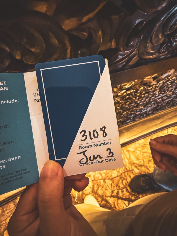 A hand holding a room-card sleeve against a decorative background.