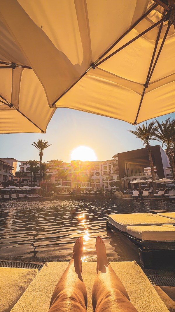 A guest’s view of a sunlit pool from beneath a large umbrella.