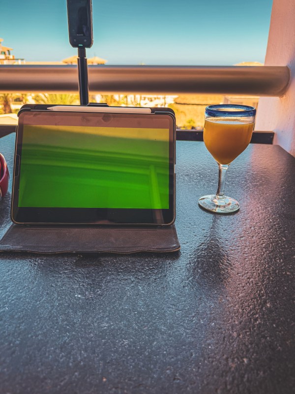 A tablet on a table beside a drink, with a sunny outdoor view.