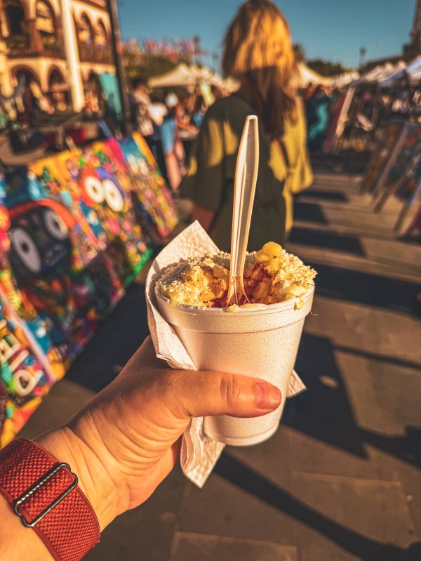 A hand holding a frozen dessert on a busy Los Cabos street.