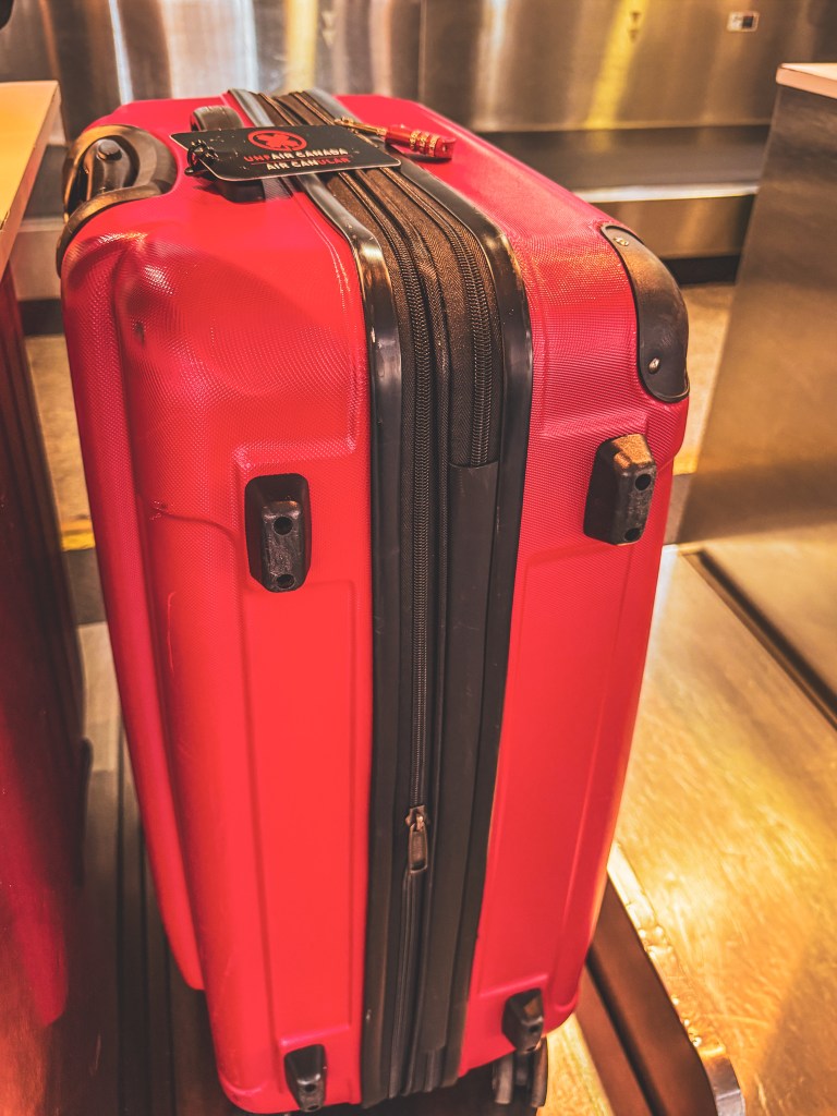 A red wheeled suitcase standing upright indoors.