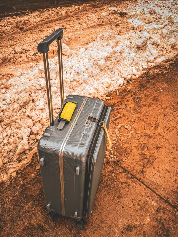 A wheeled suitcase standing on a rocky outdoor surface.