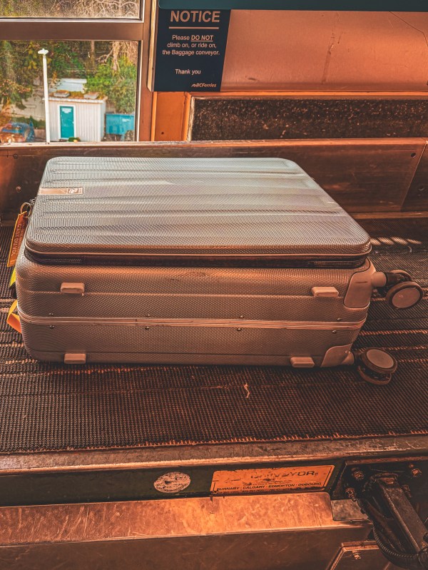 A dark hard-shell suitcase on a luggage conveyor.