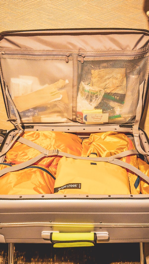 An open suitcase with clothes organized into packing compartments.