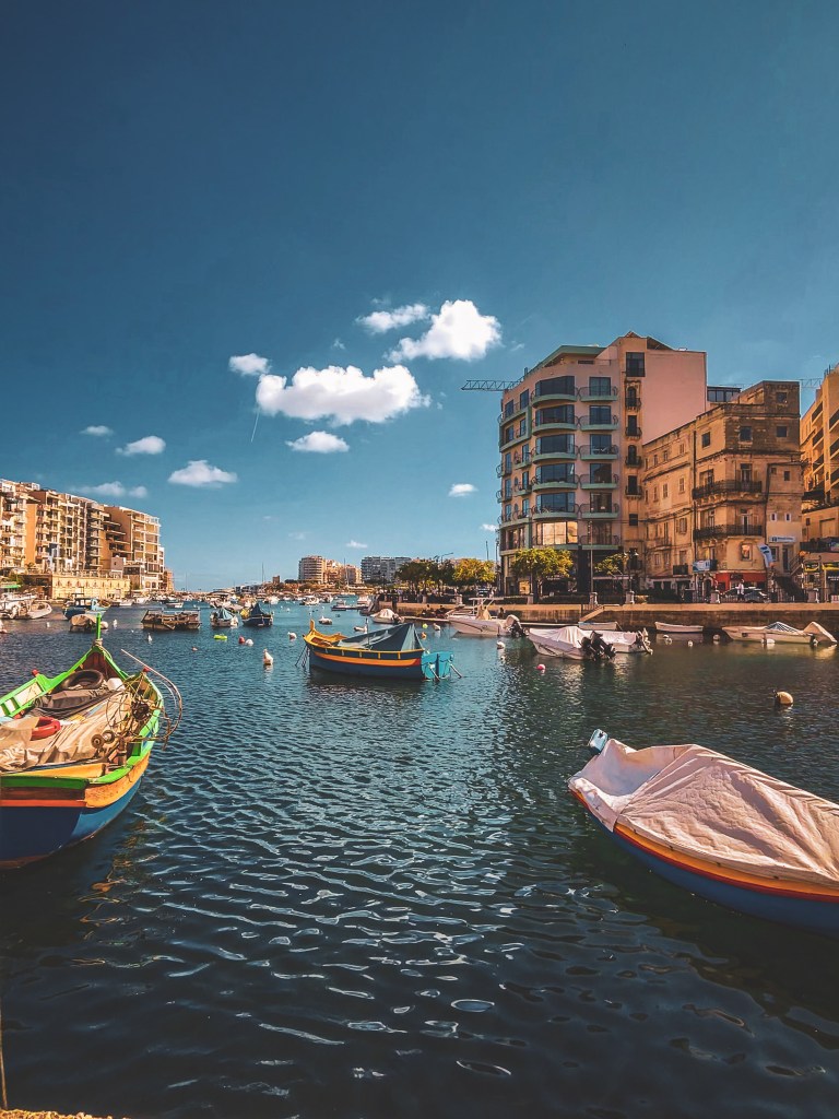 Boats and waterfront buildings beside a Malta harbour.