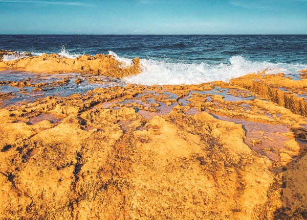 A rocky shoreline beside blue water and breaking waves in Malta.