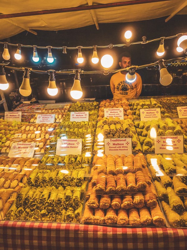 A brightly lit food stall with displayed produce and hanging lights in Malta.