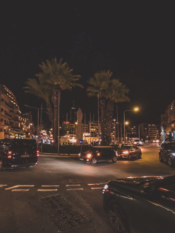A palm-lined Malta street with traffic at night.