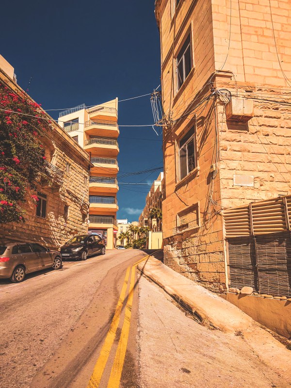 A narrow sunlit lane between stone buildings in Malta.