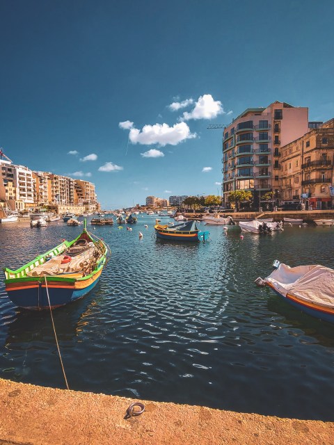 Colourful boats in a Malta harbour beneath a blue sky.