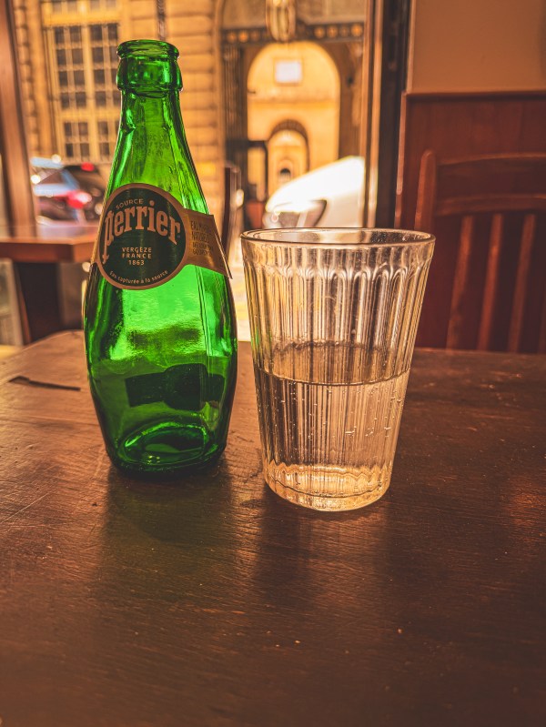 A green Perrier bottle and glass of water on a Paris table.