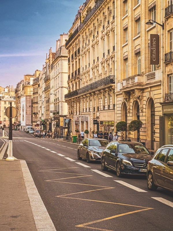 Paris street lined with stone buildings and parked cars.