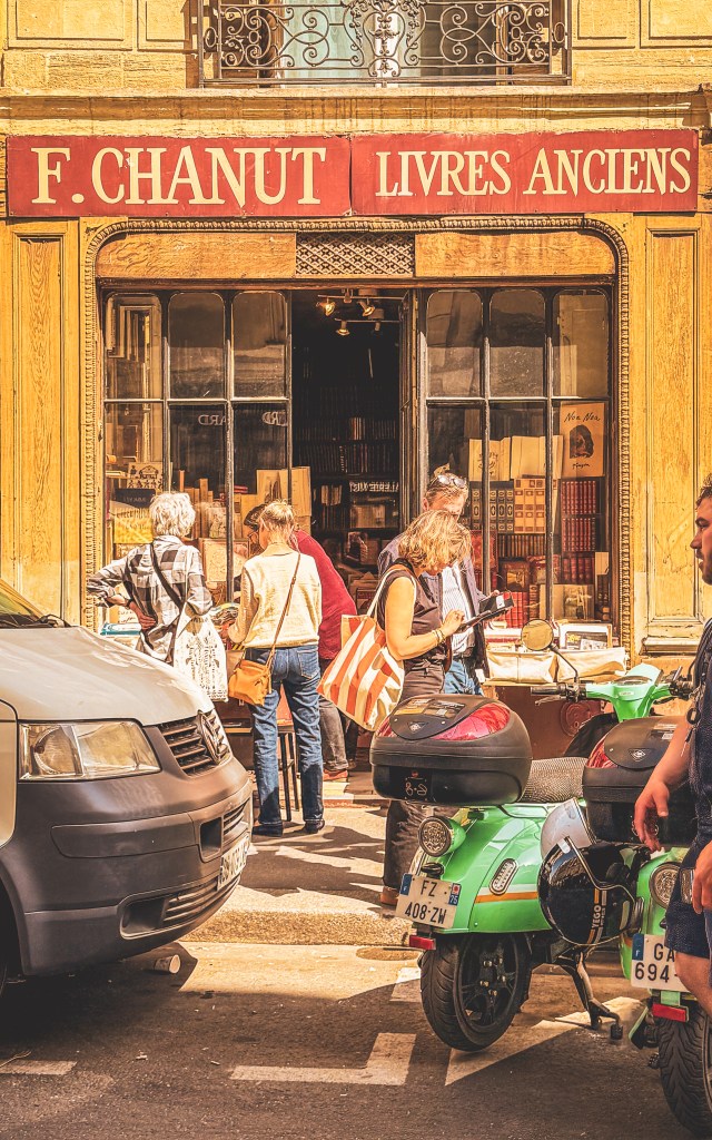 People browsing outside F. Chanut Livres Anciens, with parked scooters in a Paris street.