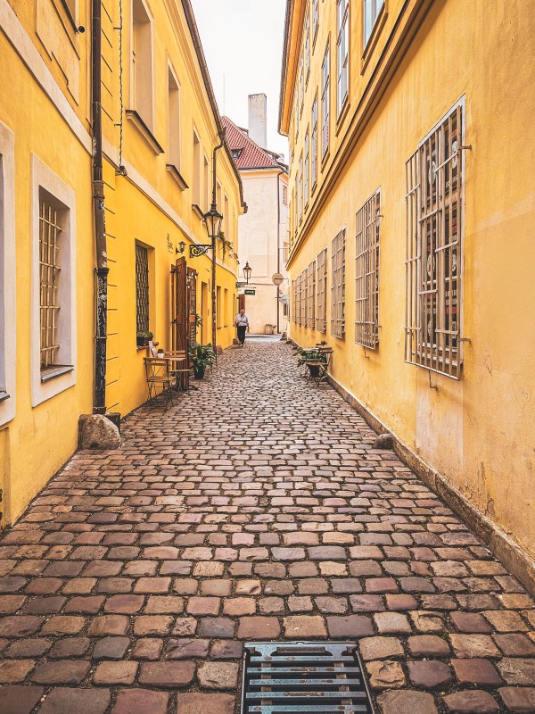 A cobbled lane between yellow buildings in Prague.