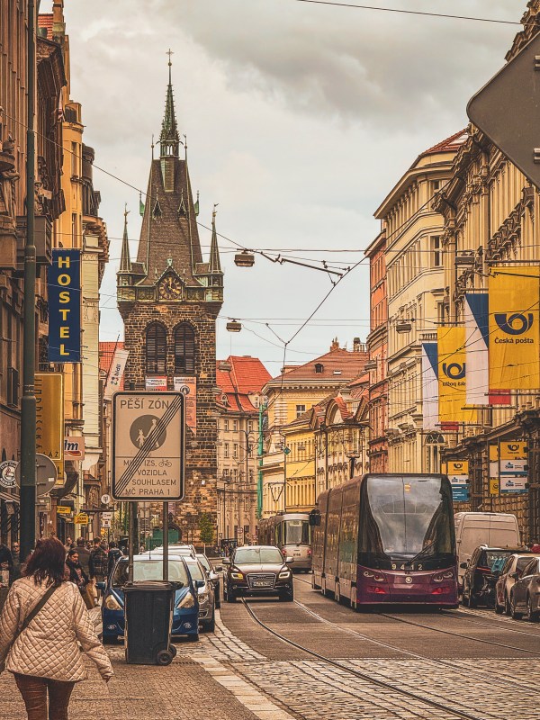 A tram moving through a Prague street beneath a tower.