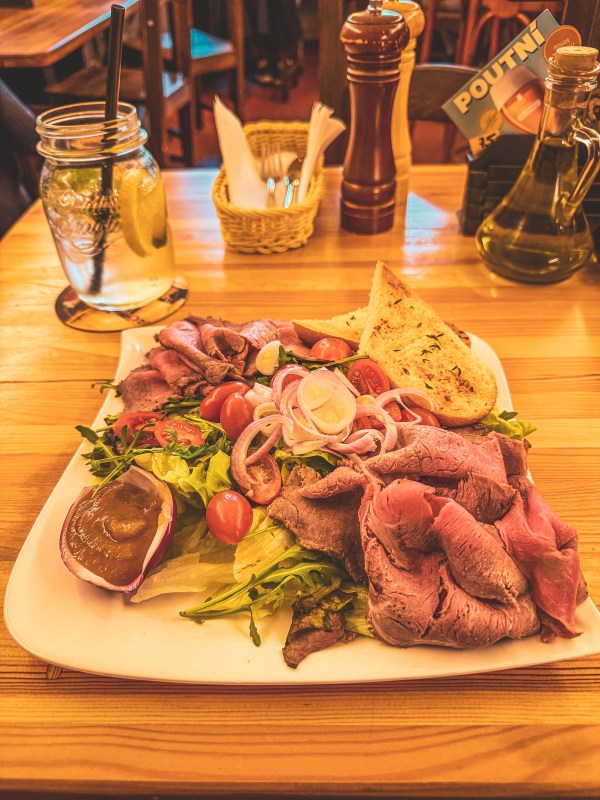 A plated meal with sliced meat and vegetables on a restaurant table in Prague.