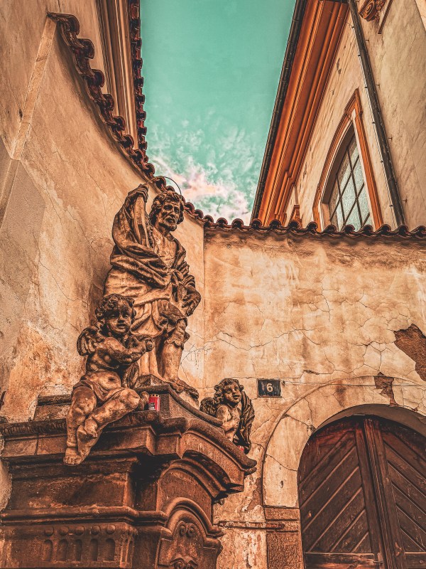 A carved stone figure beside a doorway and wall in Prague.