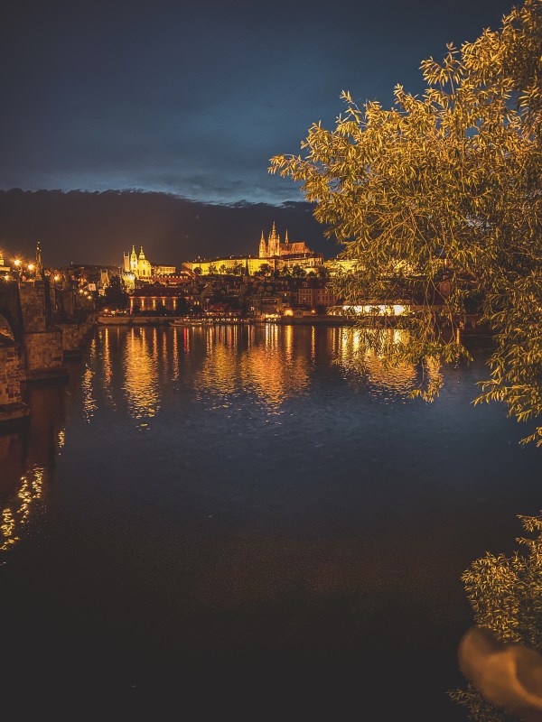 Illuminated Prague buildings reflected across the river.