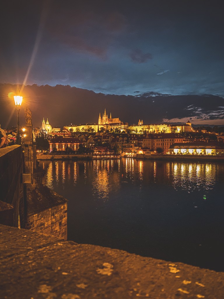 Illuminated buildings reflected in Prague’s river at night.
