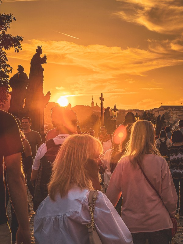 Visitors silhouetted by low sunlight on a Prague bridge.