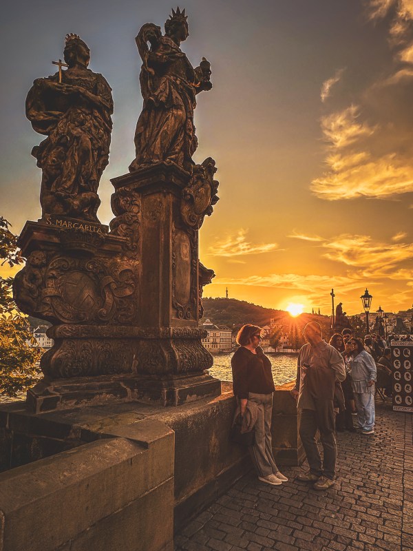 Bridge statues and visitors beneath a sunset in Prague.