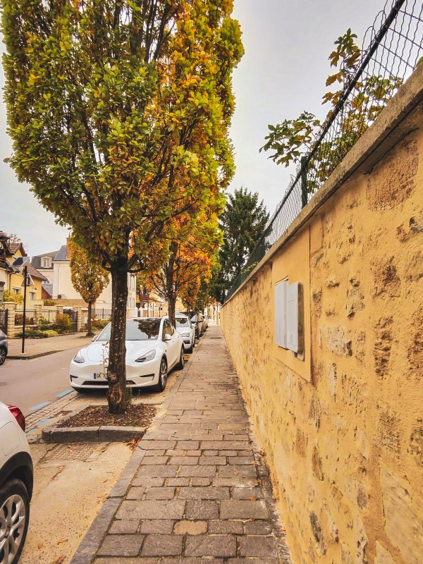 A tree-lined pavement beside a yellow wall in Roissy-en-France.