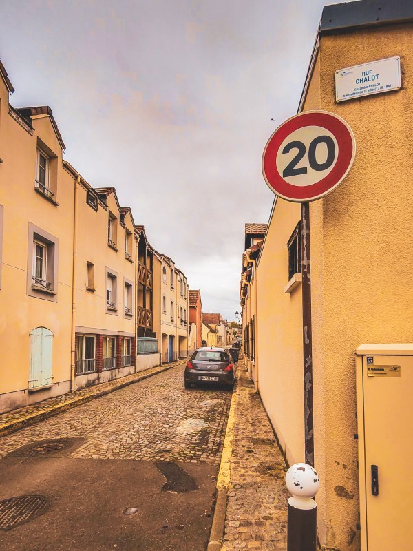 A narrow Roissy-en-France street with a speed-limit sign.