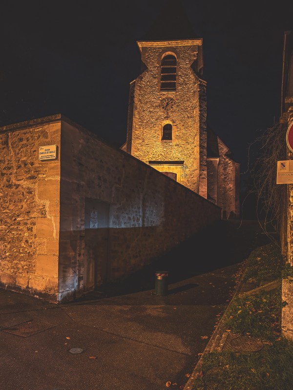 A stone tower and buildings illuminated at night in Roissy-en-France.