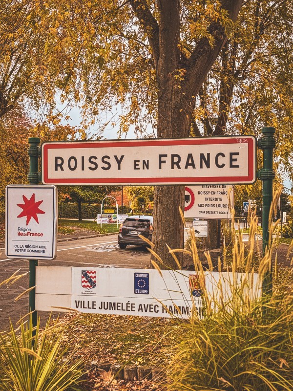 A Roissy-en-France sign framed by autumn trees.