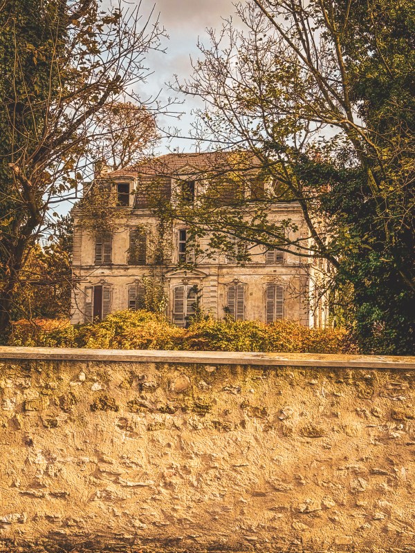 A stone building behind a wall and autumn trees in Roissy-en-France.