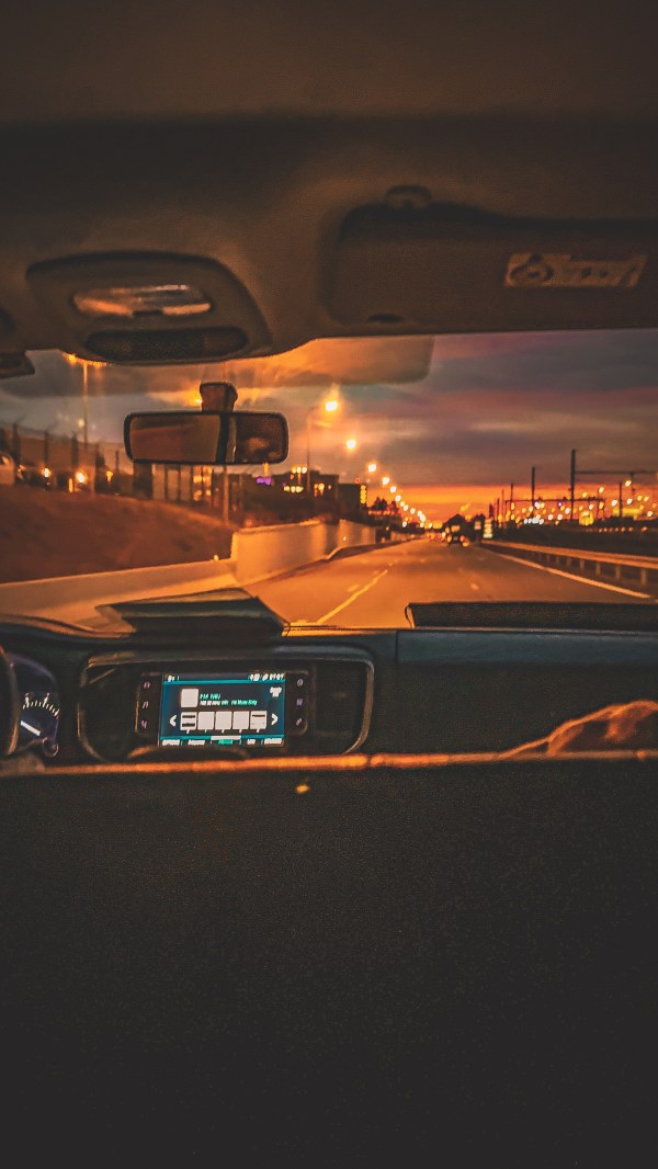 View through a vehicle windscreen on a lit road at night.