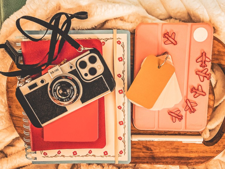 A passport, camera and notebook arranged on a table.