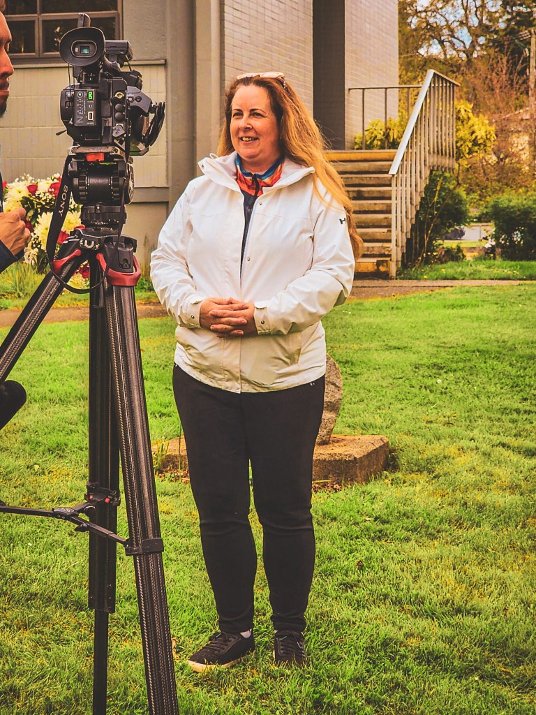 Charlotte filming outdoors with a camera on a tripod.