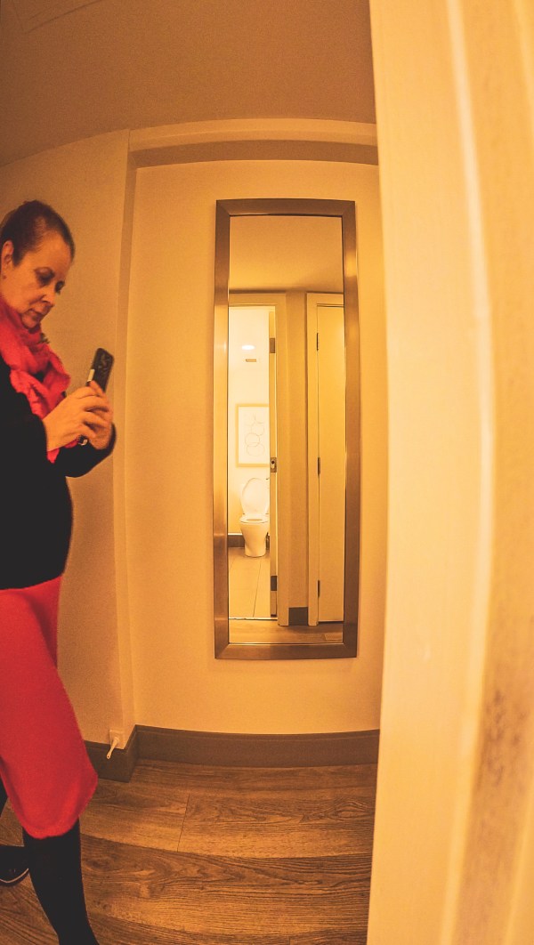 A creator holding a smartphone beside a large mirror.