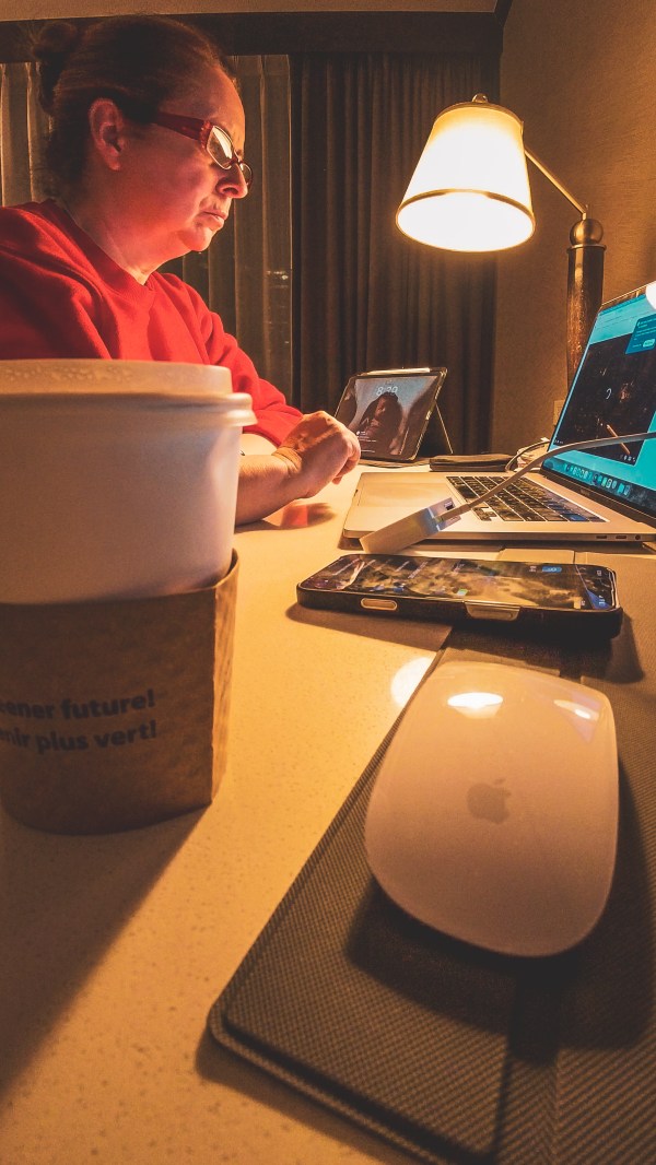A creator working on a laptop beside a lamp and coffee.