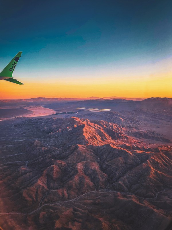 Aircraft wing above a landscape at sunset.