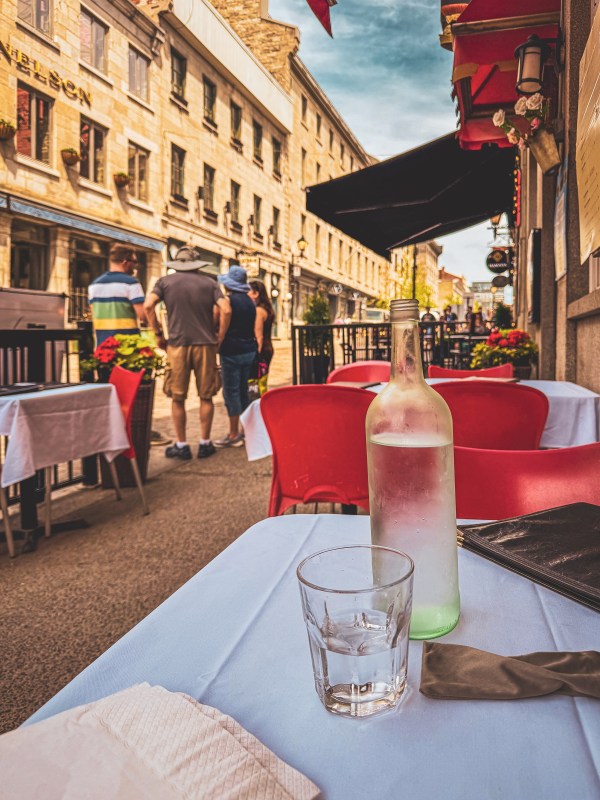 Bottle and glass on an outdoor restaurant table beside a pedestrian street.