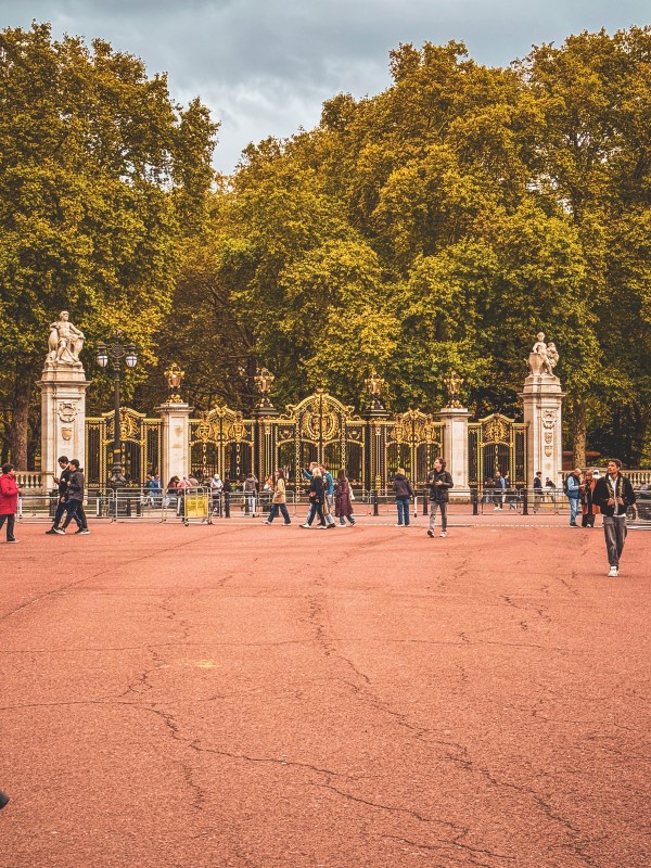 Visitors walking beside ornate gates and autumn trees.