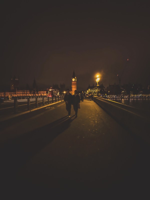 Pedestrians walking along a London bridge at night.